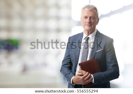 Shot of an elderly managing director with diary standing in conference room after business meeting.