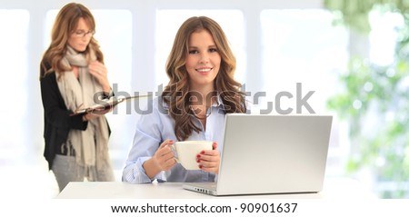 Attractive blond young business woman working on her laptop and drinking coffee in her office (blue background)