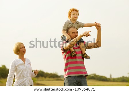 happy family having fun in the field with yellow flowers and watching up in the sky. father pointing something ahead. outdoor shot