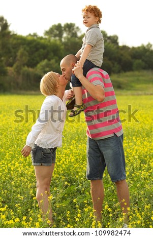 happy family having fun in the field with yellow flowers. mother and father kissing. outdoor shot
