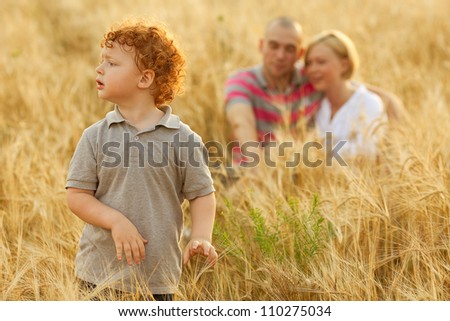 happy family having fun in the wheat field. Father and mother hug each other behind their son. Son whatching something ahead. outdoor shot