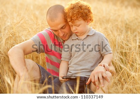 happy family having fun in the field with yellow flowers. Father hugs his son. dad and son looking at mobile device. outdoor shot