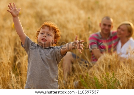 happy family having fun in the wheat field. Father and mother behind their son. Son\'s hands up. outdoor shot