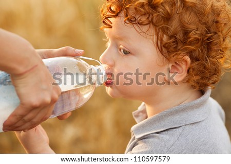 Ginger baby boy drinking water from bottle in the wheat field [Approx. 3 years]