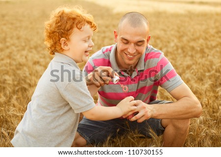 happy family having fun in the wheat field. Father doing soap bubbles to his son.