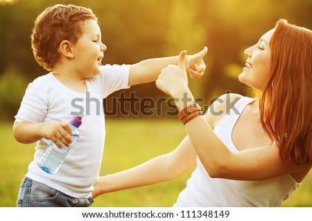 happy family having fun. baby boy with brown curly hair and  his mother with ginger hair showing thumb up each other. outdoor shot