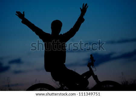 silhouette of boy cyclist in motion on the background of beautiful sunset (dawn) with hands up