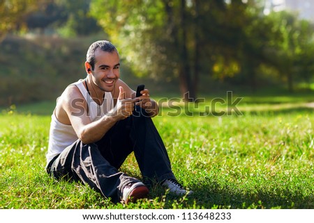 Portrait of a relaxed young man sitting on grass in park and listening to music on headphone