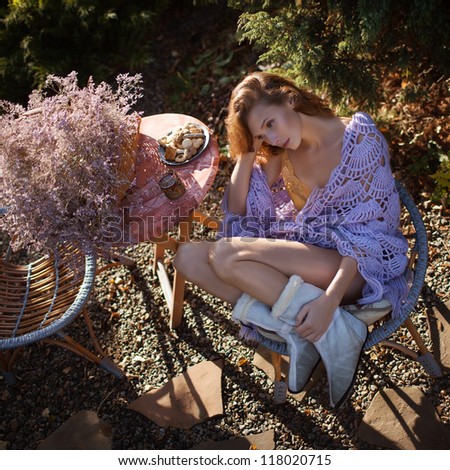 Fashion portrait of young sensual woman in garden drinking tea and sitting in the chair
