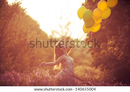 Girl have fun with yellow balloons at the sunset. Concept of freedom