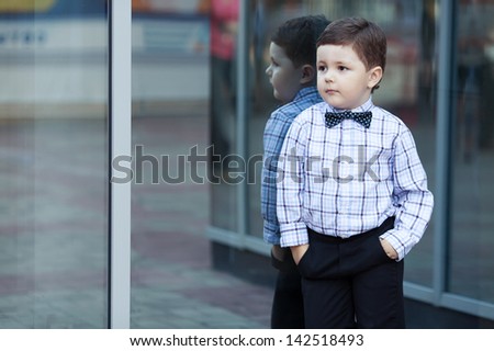 cute little stylish boy in classic style in the city close to the shop window