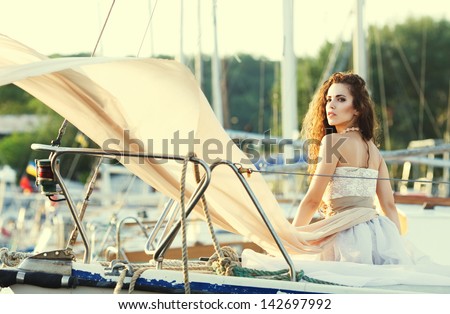 Fashion ginger model with flying dress sitting on the yacht