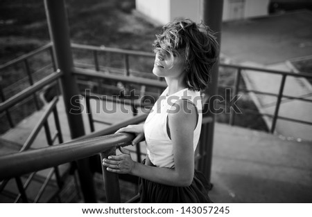 emotive portrait of girl standing on the stairs, wind blowing hairon her face, black and white