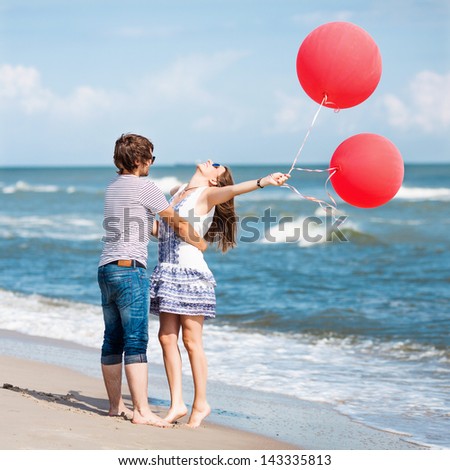 happy couple having fun on the beach, girl with open hands and  red balloons, conception of freedom