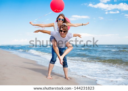 Happy Couple Having Fun On The Beach, Girl With Open Hands And Red Balloons, Conception Of Freedom