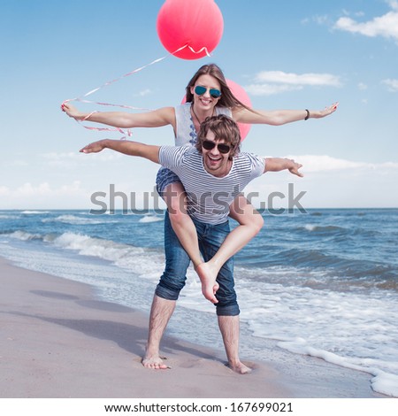 happy couple having fun on the beach, girl with open hands and red balloons, conception of freedom