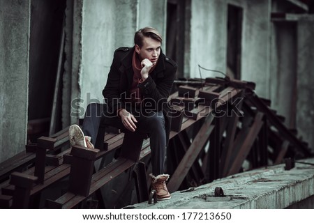fashion portrait of a stylish man posing outside, autumn time, sitting on old constructions