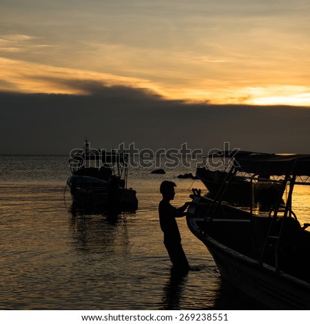 silhouette of little boat and seaman in the sea, sunset time