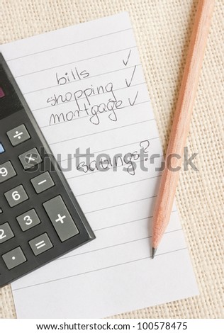 Calculator, pencil and a memo pad sheet with a list of things to pay. No money left for savings.