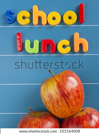 School lunch text written in magnetic letters on a blue magnetic board. Three red tasty apples underneath the text. Healthy school lunch concept.