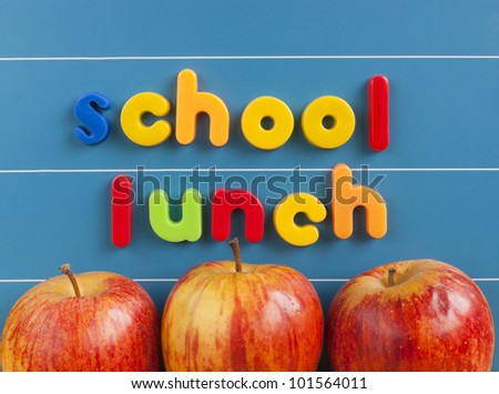 School lunch text written in magnetic letters on a blue magnetic board. Three red tasty apples placed underneath the text. Healthy school lunch concept.