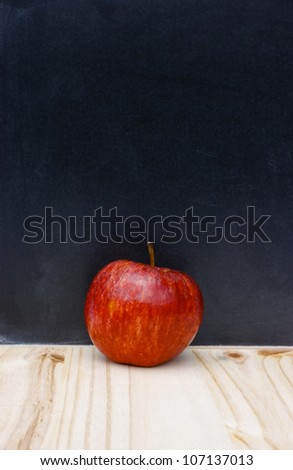 Back to school or college education concept. Red apple against a traditional authentic scratched blackboard or chalkboard. Copy space.