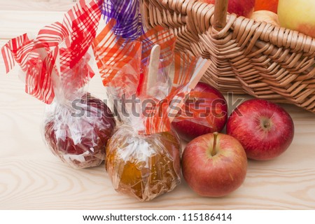 Caramel, chocolate and toffee apples wrapped up in colorful foil next to a basket of freshly picked up red apples. On a wooden table.
