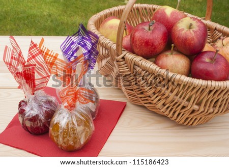 Caramel, chocolate and toffee apples wrapped up in colorful foil next to a basket of freshly picked up red apples. On a wooden table in the garden. Natural light.
