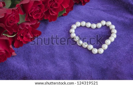 Pearl bracelet in a shape of a heart on a vintage purple velvet with bunch of red roses. Concept for a Valentine\'s Day gift. Copy space.