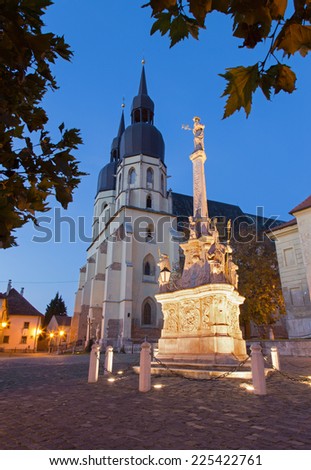 Trnava - The gothic Saint Nicholas church and baroque column of st. Joseph at dusk.