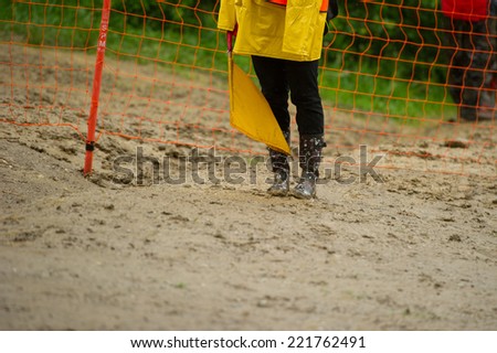 Person standing in mud with muddy boots holding red flag.