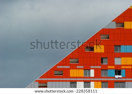 Modern apartment building in the city with orange and red facade in the shape of a triangle.