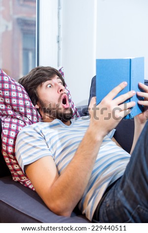 Caucasian student man reading a book with a surprised expression on his face.
