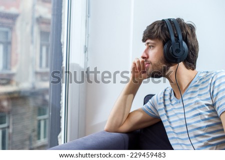 Student man listening to music while looking through the window and wondering.