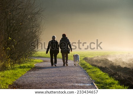 Two middle aged women walking a dog on a path in a park.