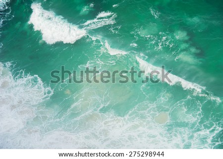 Ocean waves shot from above. The water is turquoise color and the waves have a diagonal path.