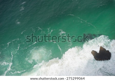 Ocean waves shot from above. The water is turquoise color and you can also see a rock.