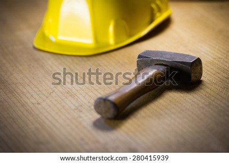 Sledgehammer on a wooden board with a yellow safety helmet in the background.