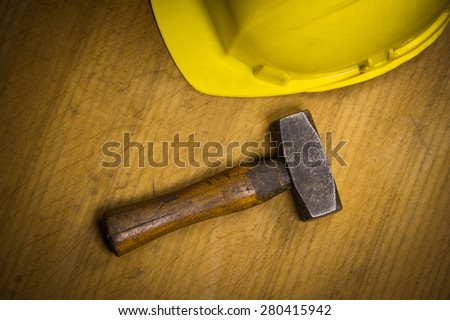 Big industrial hammer with a yellow safety helmet in the background on a dark wooden desk.