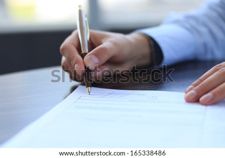 Businesswoman sitting at office desk signing a contract with shallow focus on signature