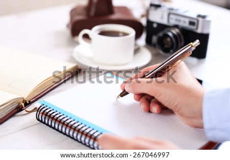 Woman makes a note in a notebook with a retro camera in the background