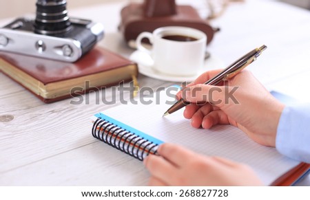 Woman makes a note in a notebook with a retro camera in the background