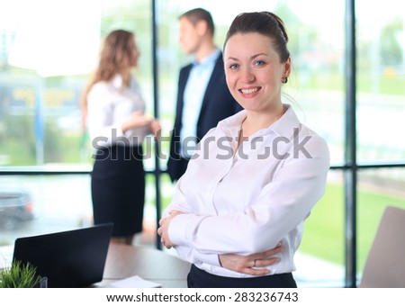 Business woman standing in foreground with a tablet in her hands, her co-workers discussing business matters in the background