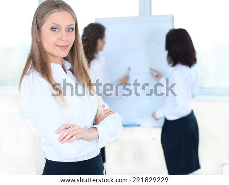 Business woman standing in foreground and her co-workers discussing business matters in the background