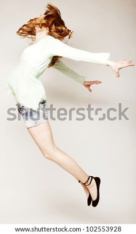 Portrait of a beautiful young lady jumping in joy over grey  background