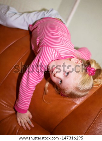 Portrait of a little blonde girl lying on the back of couch