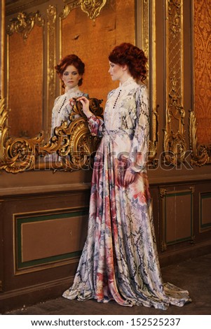 Young Beautiful Woman Standing In The Palace Room With Mirror.