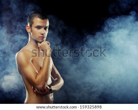 Portrait of a muscular male model against dark  background with smoke.