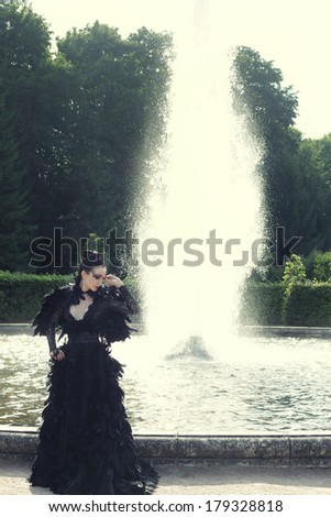 Fashion model posing next fountain in summer park. Dark Princess.