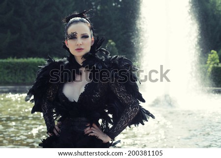 Fashion model posing next fountain in summer park. Dark Princess.